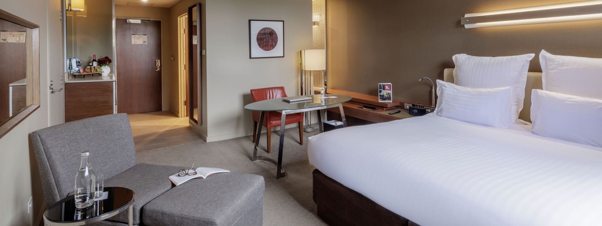 Work desk by the bed with a Lounge chair and carpet floors in the Pullman Superior King Room at Pullman Sydney Olympic Park