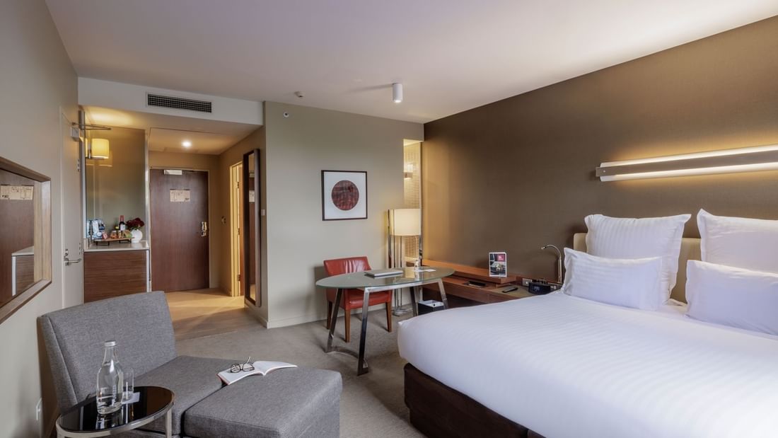 Work desk by the bed with a Lounge chair and carpet floors in the Pullman Superior King Room at Pullman Sydney Olympic Park