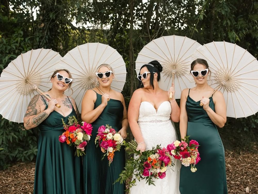 Four bridesmaids and bride in green and white dresses holding colorful bouquets and umbrellas.