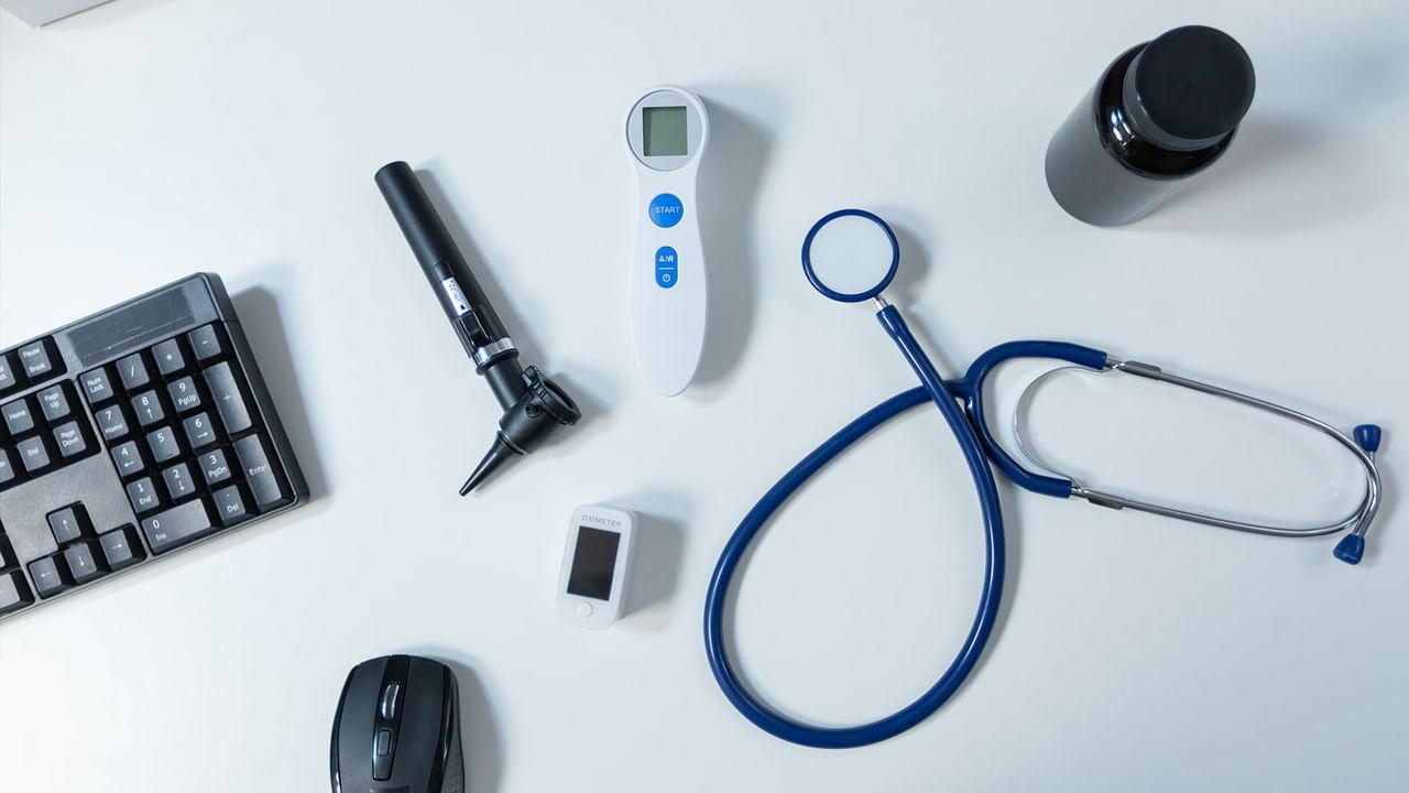 A white table displays a stethoscope, thermometer, otoscope, keyboard, mouse, and a small device.