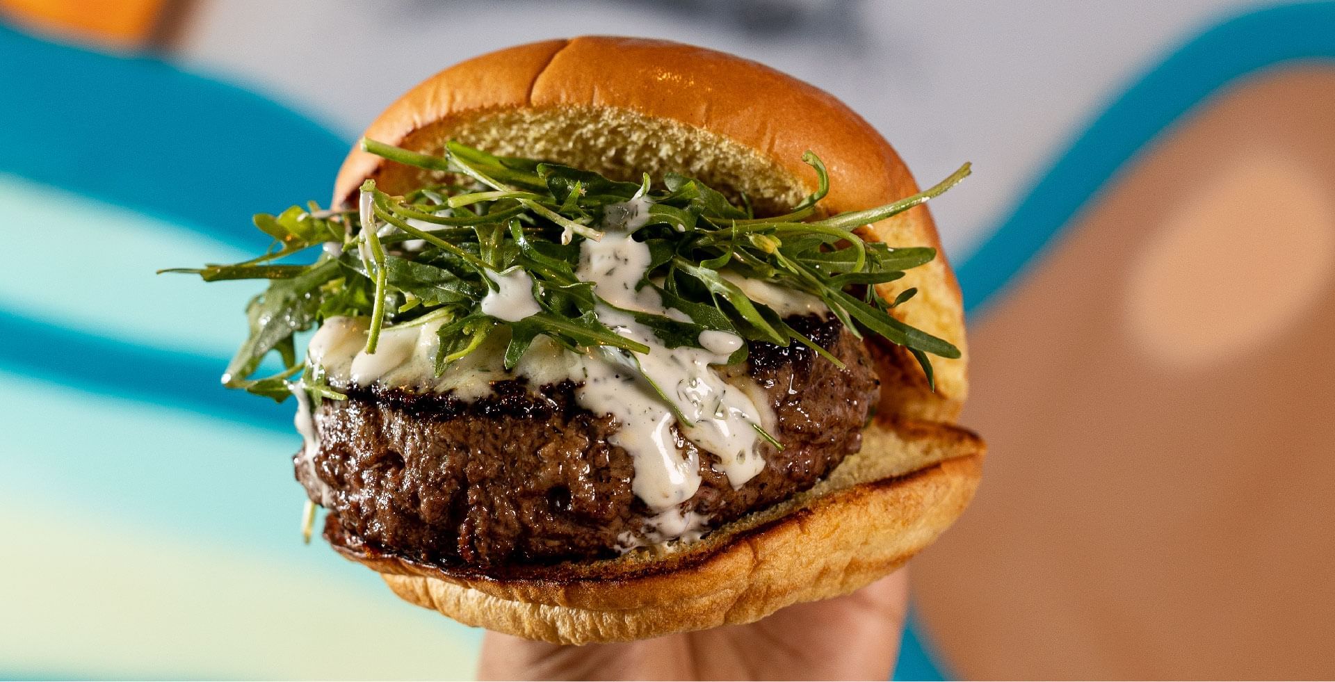 A large, gourmet burger with arugula and white sauce, held at Sunway Resort