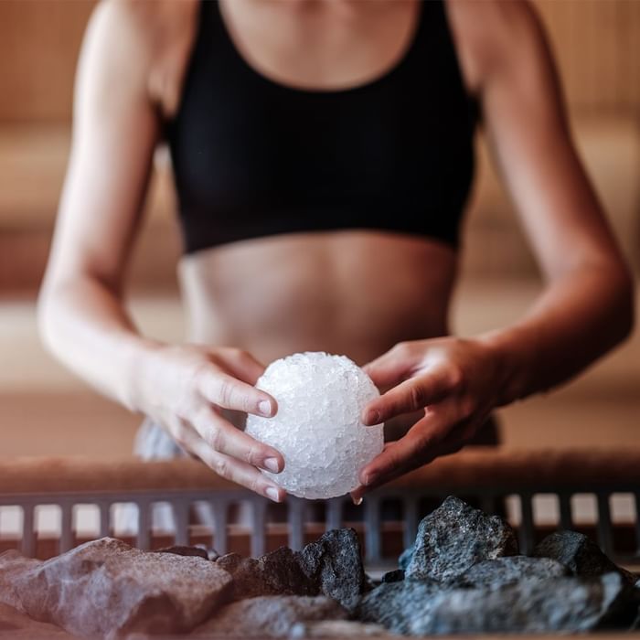 Frau in schwarzem Sport-BH hält weißen Eiskristall über Körbchen mit dunklen Steinen.