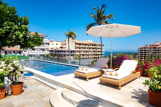 Luxury rooftop swimming pool deck with comfortable lounge chairs and a white umbrella at Playa Los Arcos Beach Resort & Spa