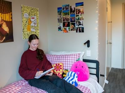 Student reading on bed in personalized room with posters, photos, and colorful pillows at Tupuārangi