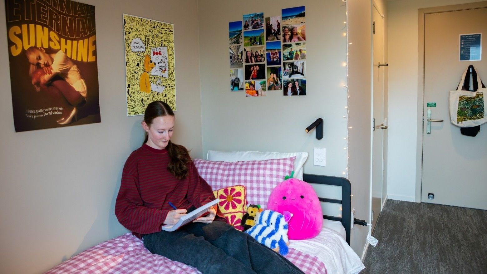 Student reading on bed in personalized room with posters, photos, and colorful pillows at Tupuārangi