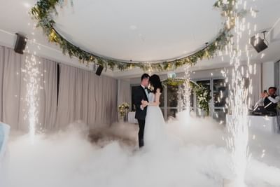 Couple sharing a first dance amid a dreamy, fog-filled room adorned with sparks and greenery at Amora Herencia Riverwalk