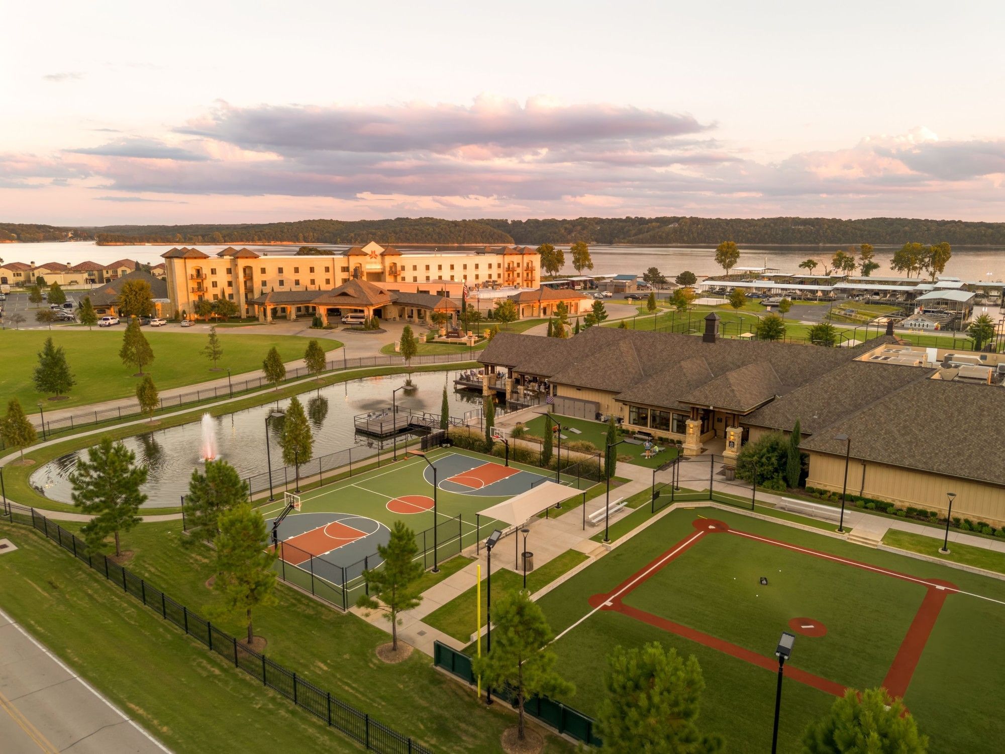 Aerial view of basketball and tennis courts beside a pond at a resort during sunset at Shangri-La Resort and Golf Club