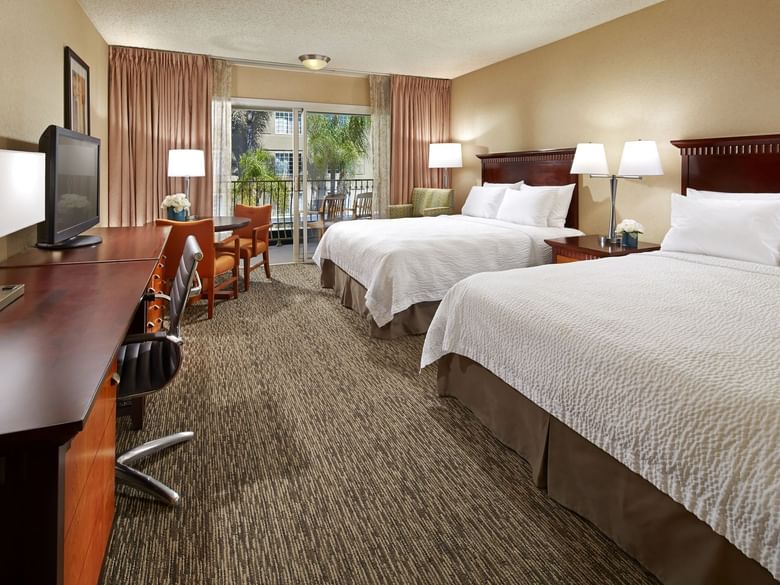 A hotel room with two beds, a desk, and a balcony