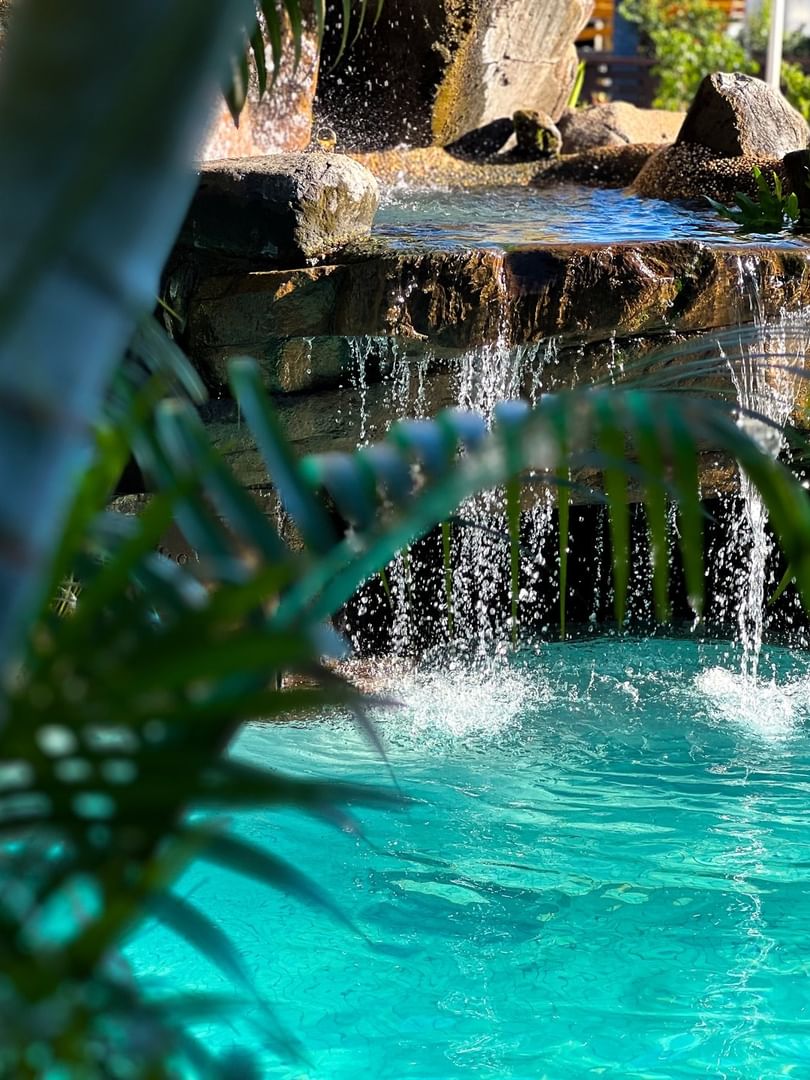 Waterfall flowing into a swimming pool surrounded by lush greenery at Tokatoka Resort - Fiji International Airport in Nadi