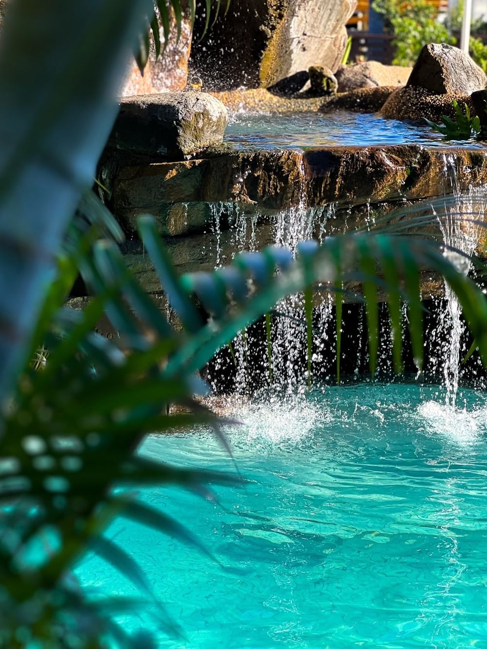 Waterfall flowing into a swimming pool surrounded by lush greenery at Tokatoka Resort - Fiji International Airport in Nadi.