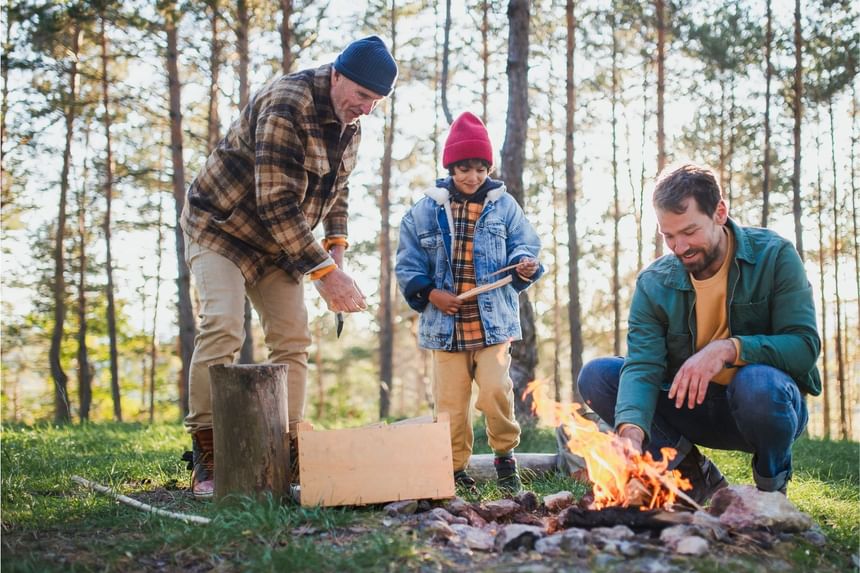 Two men and a child camping in a forest, gathered around a campfire, roasting marshmallows at Fall Creek Marina & Campground