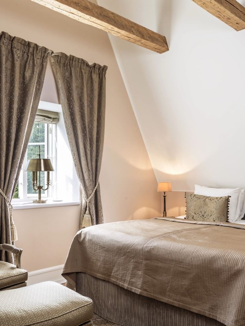 Deluxe room featuring exposed ceiling beams and armchair & ottoman with large bed at Warwick Denmark