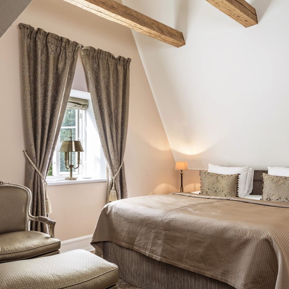 Deluxe room featuring exposed ceiling beams and armchair & ottoman with large bed at Warwick Denmark
