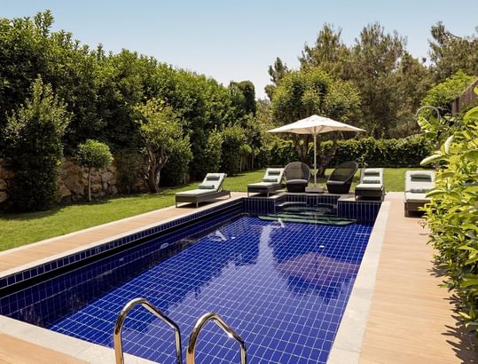 Exclusive Villa's private outdoor pool with lounge chairs, umbrella, and greenery at Titanic Luxury Collection Bodrum.