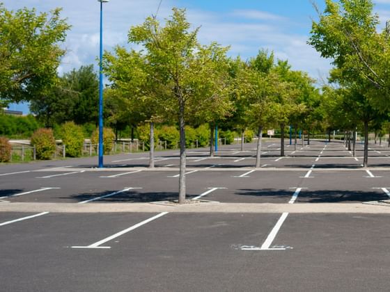 An empty parking lot lined with young trees and blue poles under a sunny sky at Hotel des Innovations