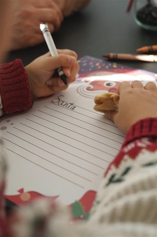 Child writing a letter to Santa on festive stationery by crayons and holiday decorations on a table at Hotel X Toronto