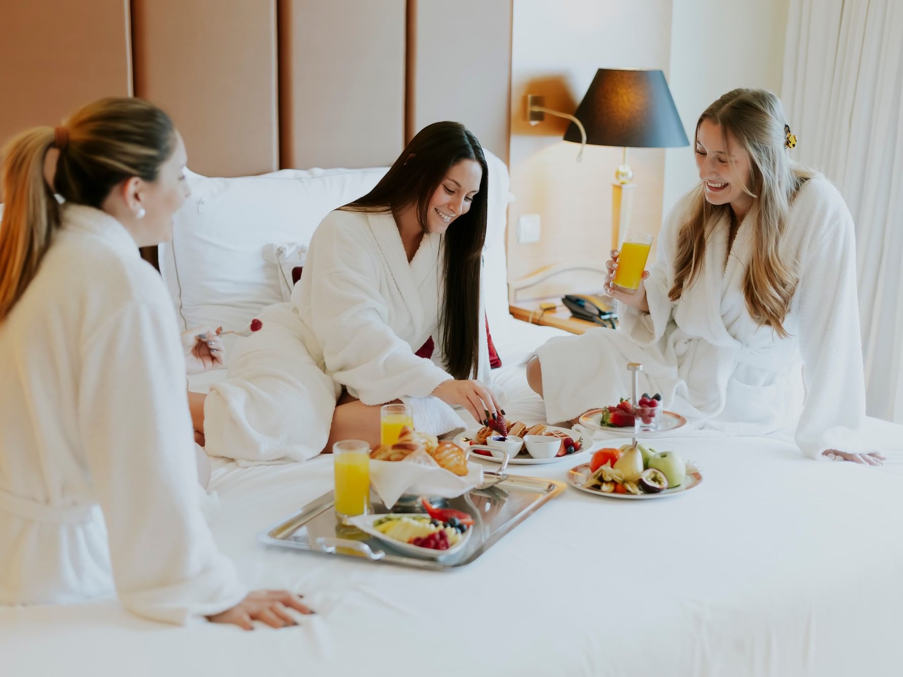 Trois amies en peignoirs profitent d'un petit-déjeuner en chambre lors d'une ecapade de copines en Cascais.
