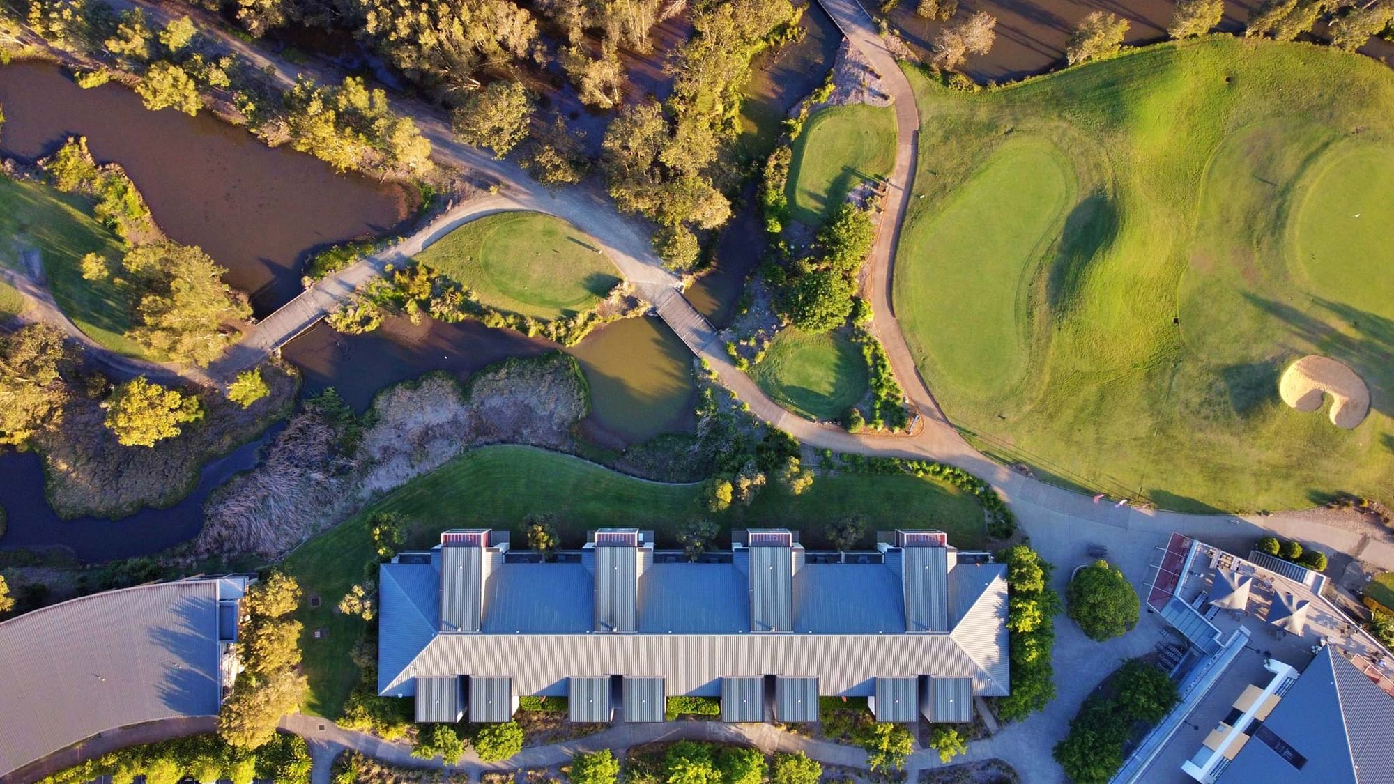 Aerial view of a golf course with ponds, pathways, and a large building with a curved roof.
