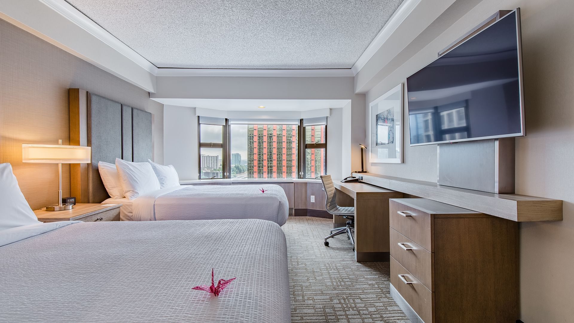 A hotel room with two double beds, a desk, TV, and window.
