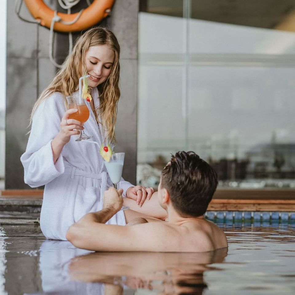 Pasangan berpose dengan koktail di tepi kolam renang di LK Cikarang Hotel & Residences