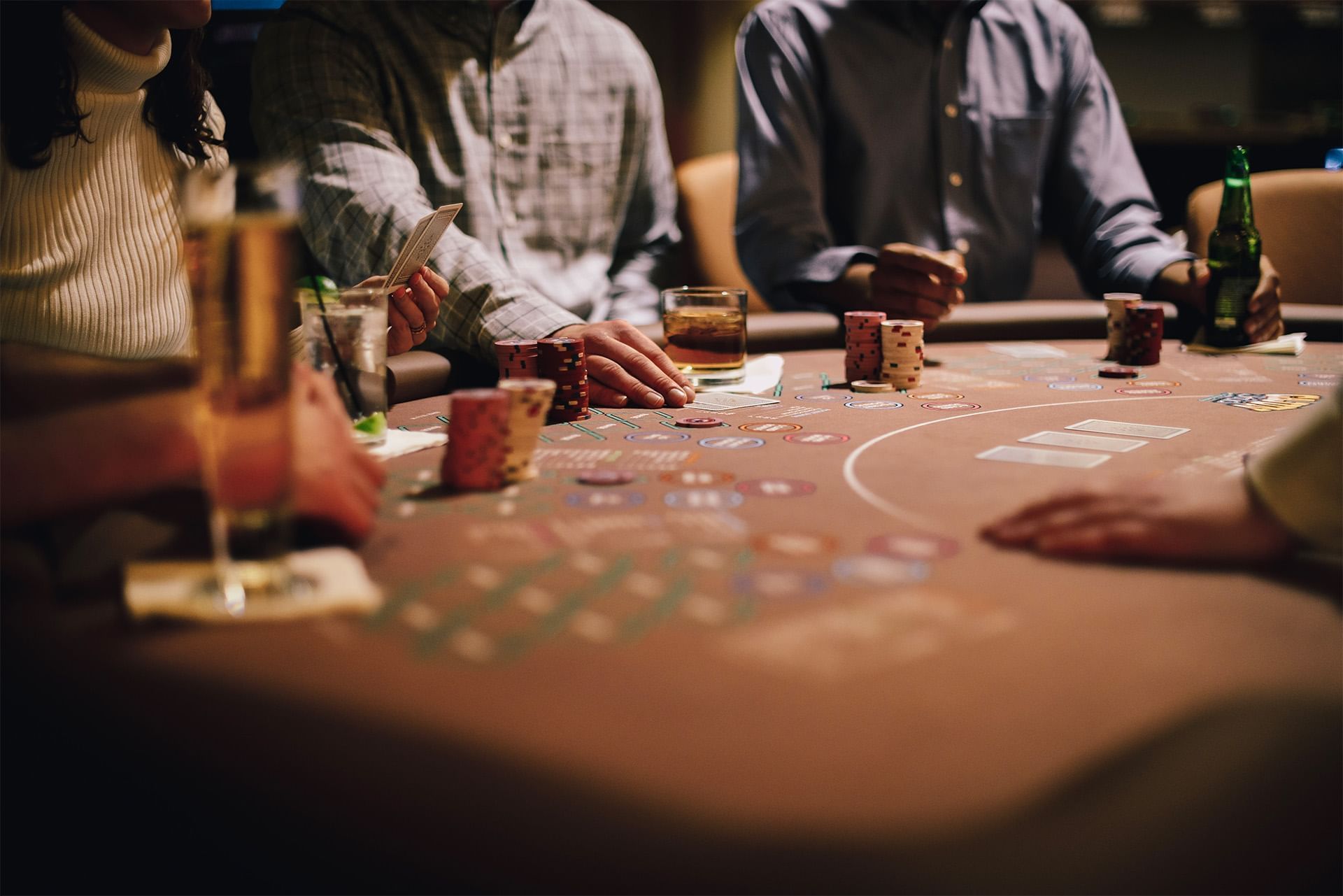Guests play casino cards around a gaming table with stacked poker chips and drinks under warm lighting at The Brook