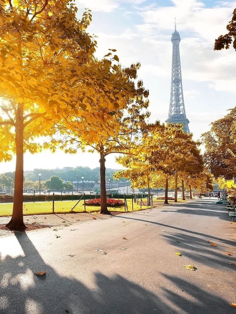 Park pathway with benches placed by autumn trees, with the Eiffel Tower in the distance near Warwick Hotels & Resorts