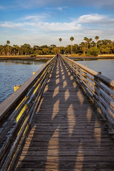 Wooden pier over calm water with long shadows and a lush greenery backdrop near The J Hotel