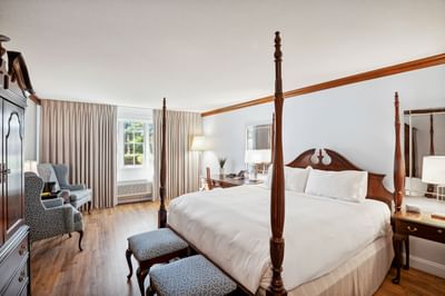 Four-poster bed with a bench beside two armchairs near the window in Traditional King at Avon Old Farms Hotel