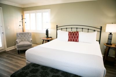 A neatly made bed with white sheets and pillows, a gray armchair, and two nightstands with lamps.