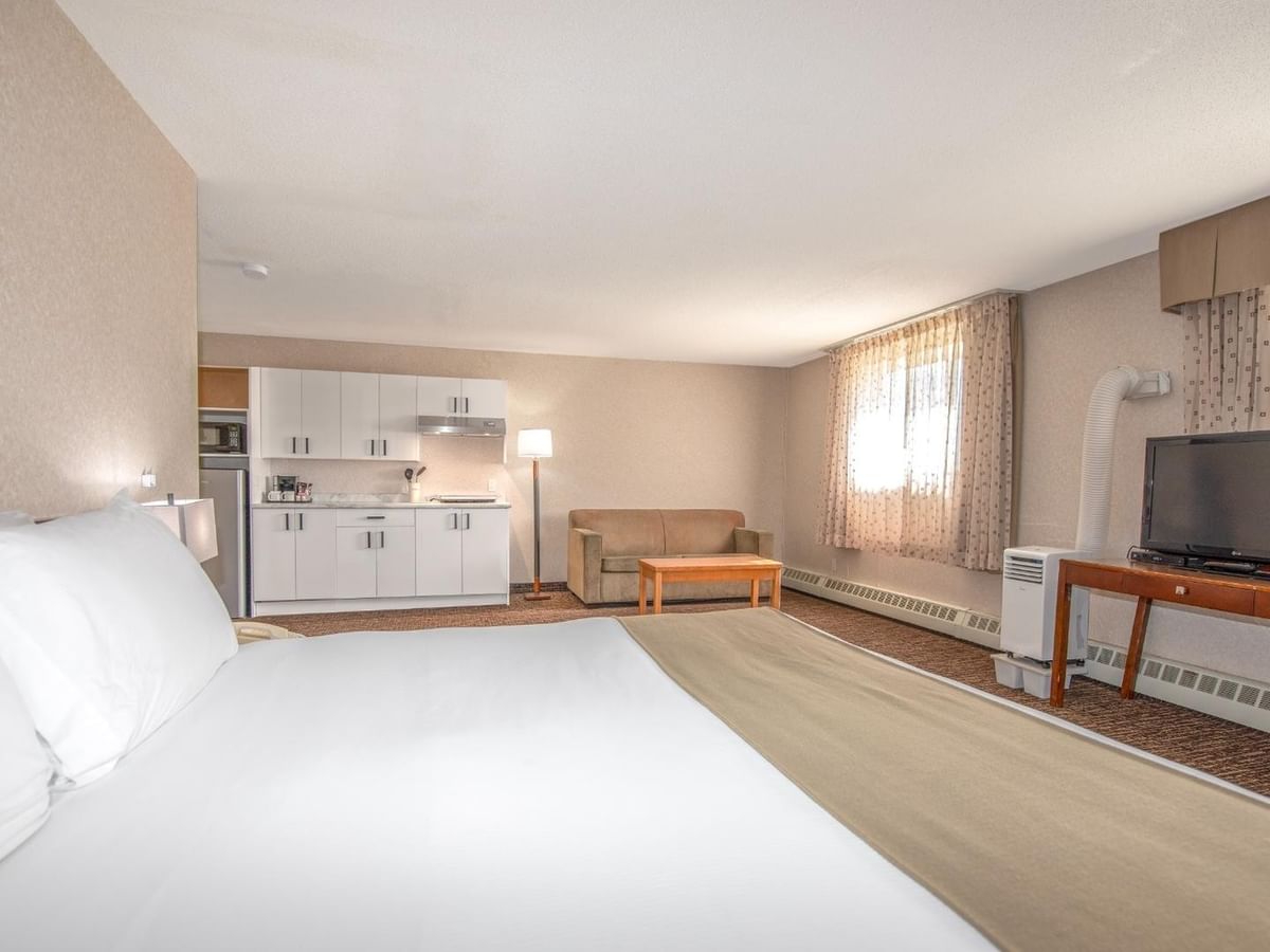 A hotel room with a king bed, kitchenette, couch, TV, and artwork on the wall.