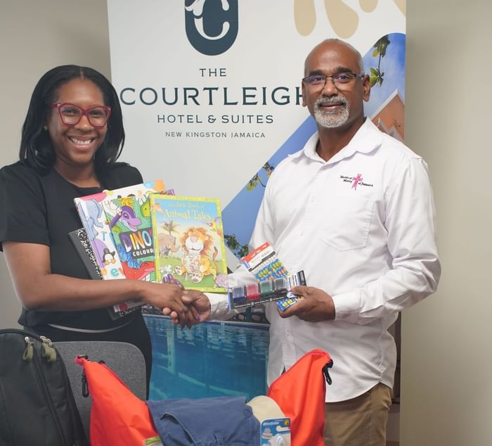 Man and a woman shaking hands over school supplies at Courtleigh Hotel & Suites, a featured hotels in Kingston, Jamaica