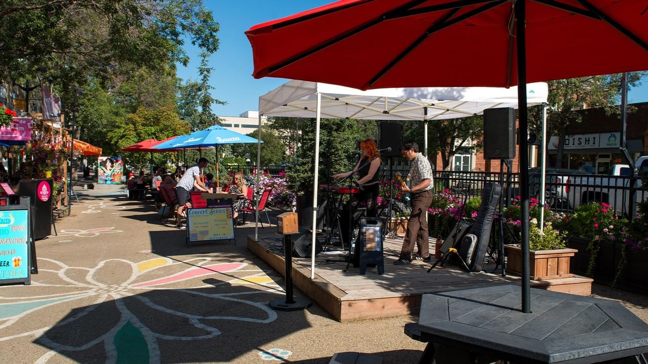 Outdoor pedestrian street with colorful umbrellas, live music stage, and shops in Downtown Red Deer on a sunny day.