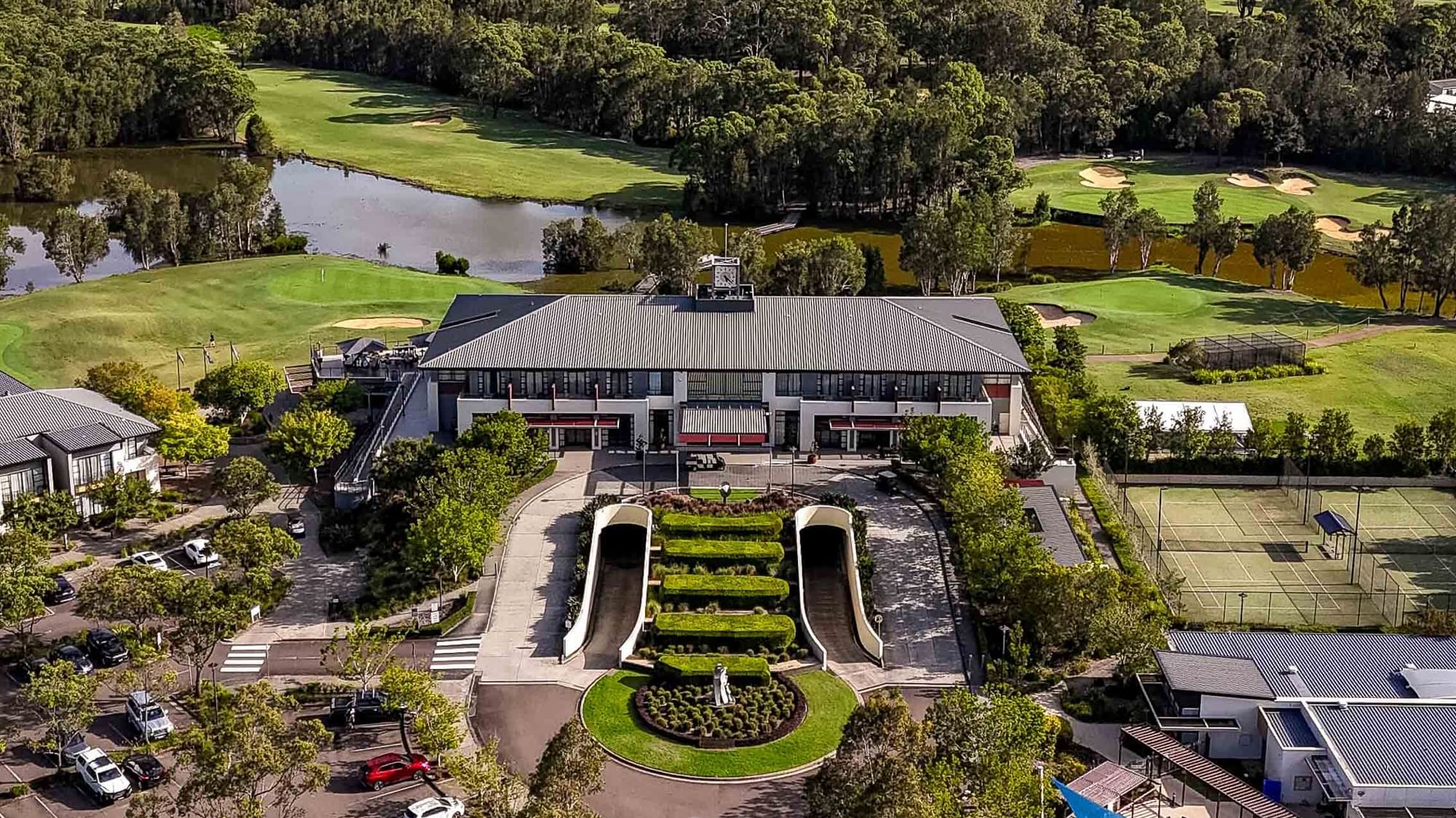Aerial view of a resort with buildings, tennis courts, landscaped gardens, and a golf course.