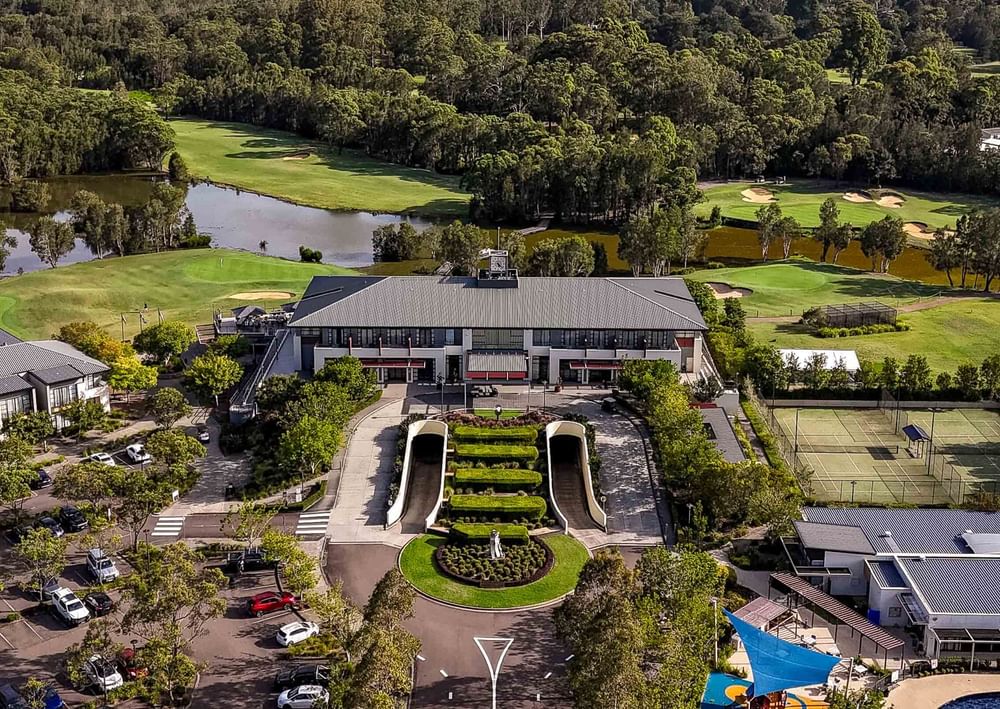 Aerial view of Mercure Kooindah Waters golf resort with buildings, tennis courts, and lush greenery