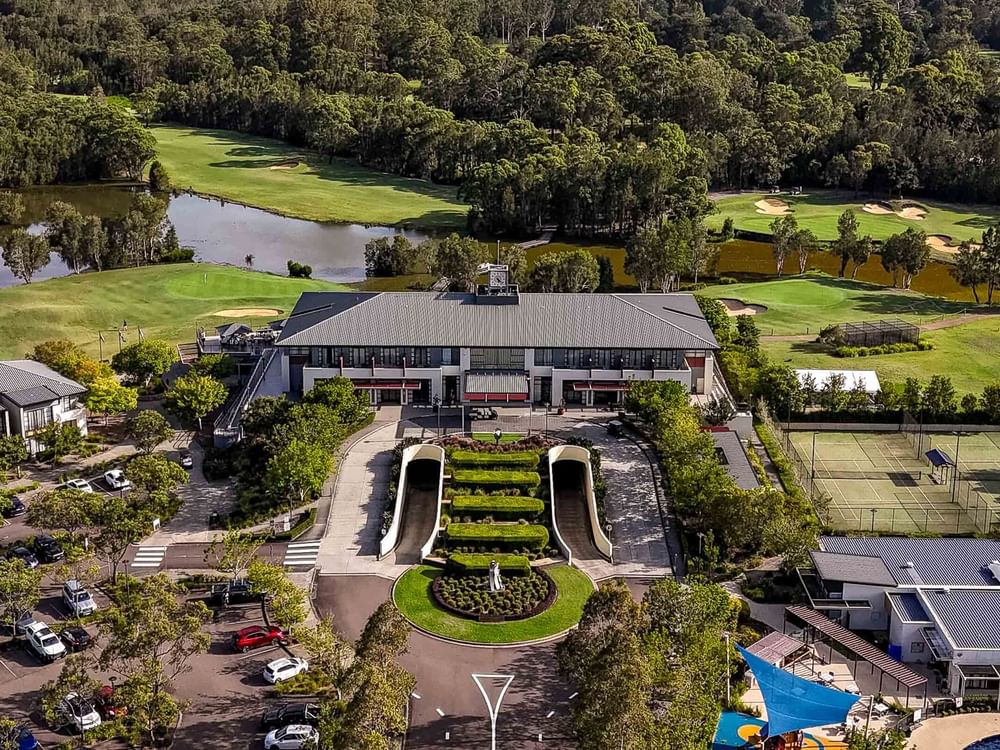 Aerial view of a resort with a large building, golf course, tennis courts, parking lot, and lush greenery.