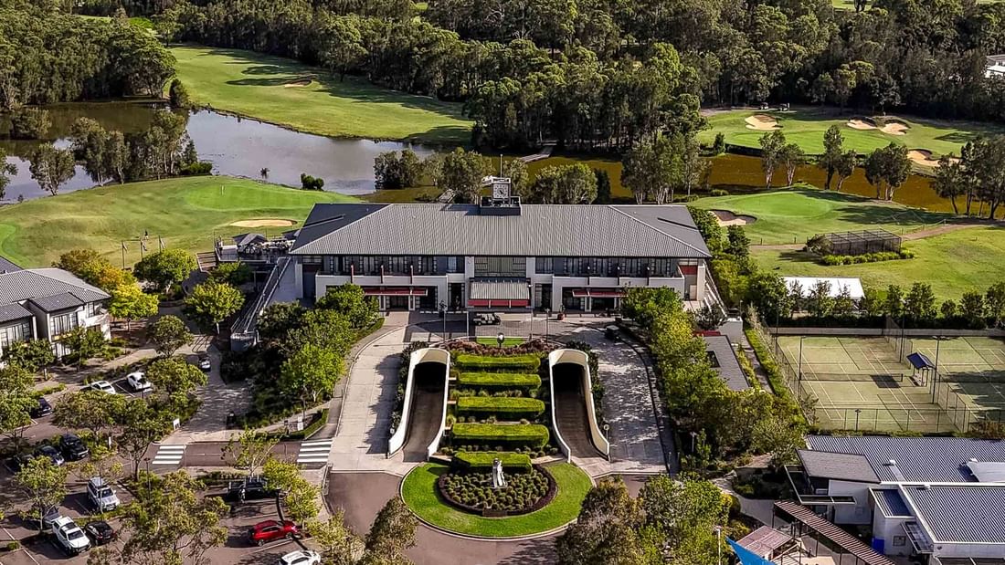 Aerial view of a resort with a large building, golf course, tennis courts, parking lot, and lush greenery.
