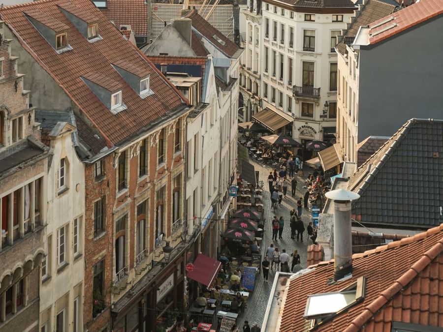 Levendige straat met terrasjes en wandelaars tussen historische gebouwen met rode pannendaken in Brussel
