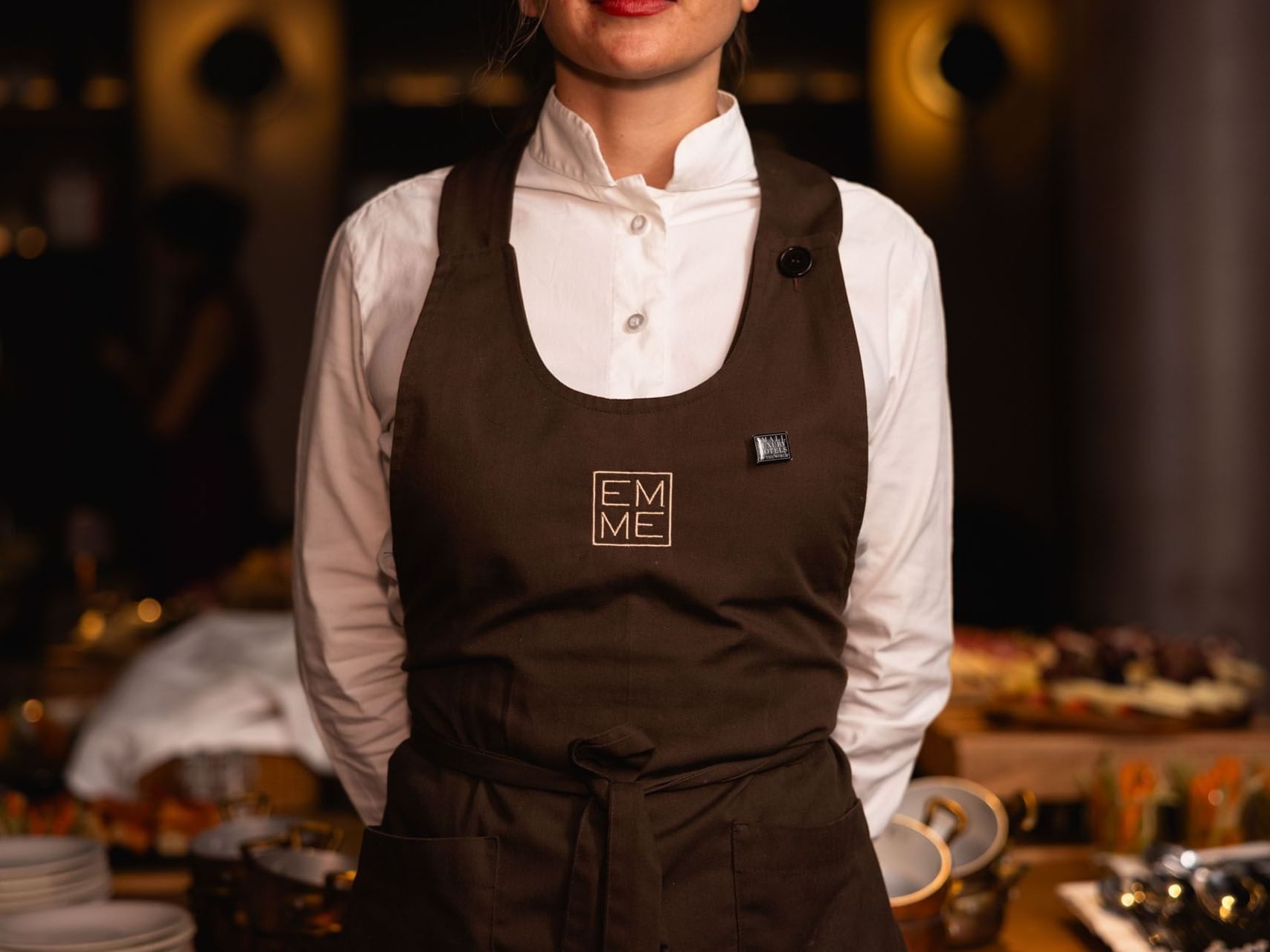 A chef in a brown apron posing to the camera at EMME Restaurant