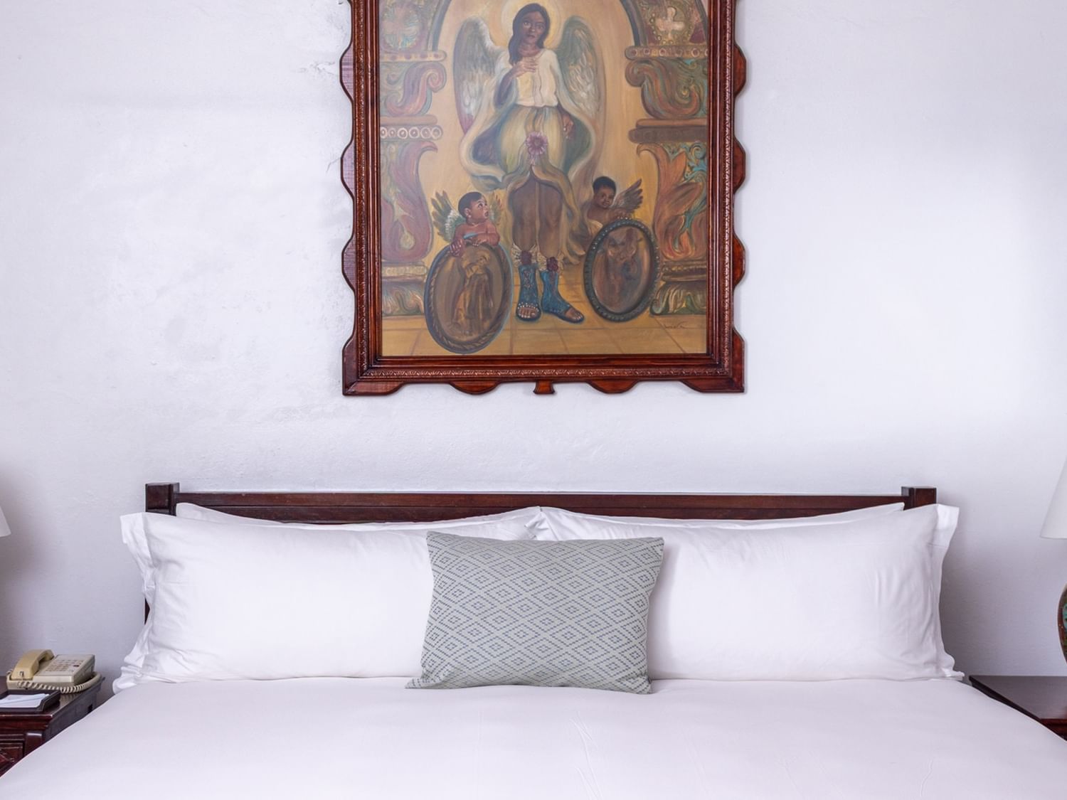White bed by a wooden headboard under a framed angel painting at Quinta Real