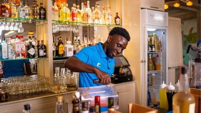 Bartender in blue polo mixes a drink using a blender at the bar counter in Sand Street Bistro at Sugar Cane Club Hotel & Spa