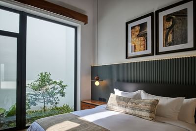 Elegant bedroom with a cozy bed, a wall light, and a glass wall showing an outdoor garden at Singular Signature Residences