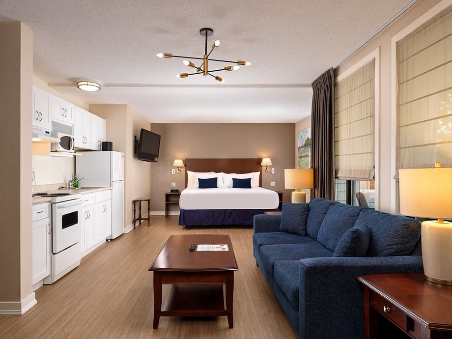 Spacious Balmoral Room with kitchen, blue sofa, and king bed at Huntingdon Hotel and Suites in Victoria.