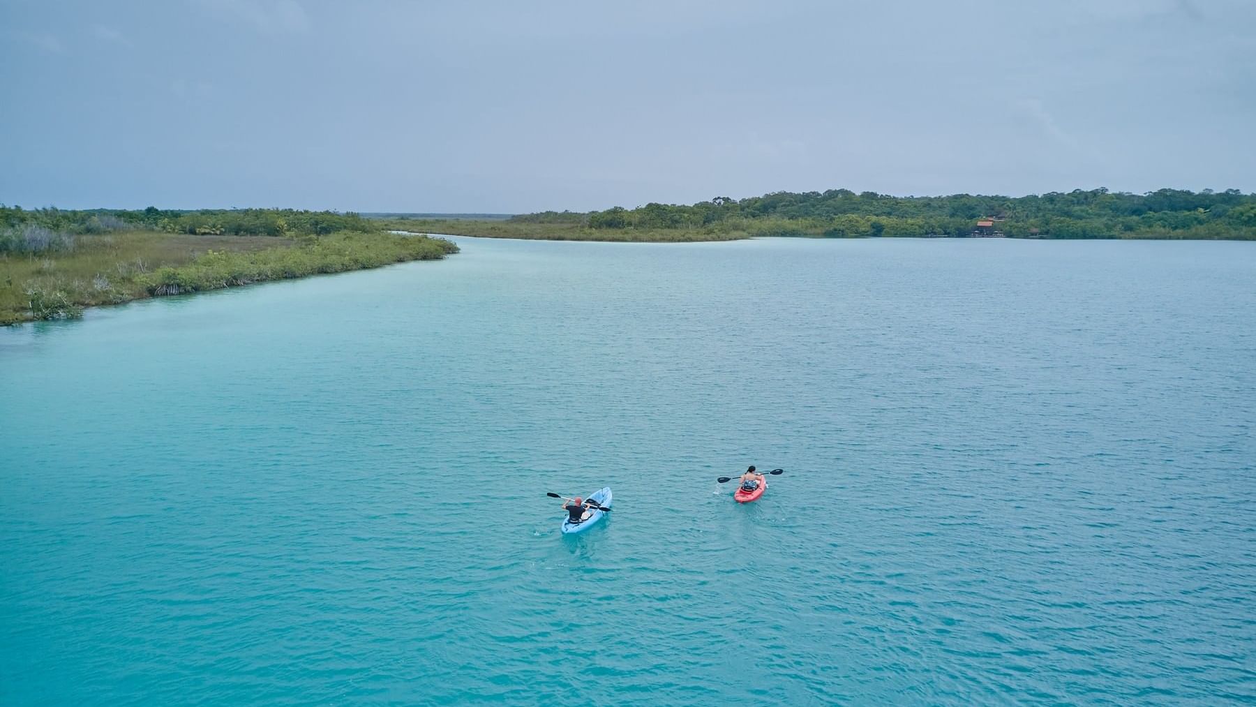 Two people kayaking on a serene blue lake near The Explorean Kohunlich