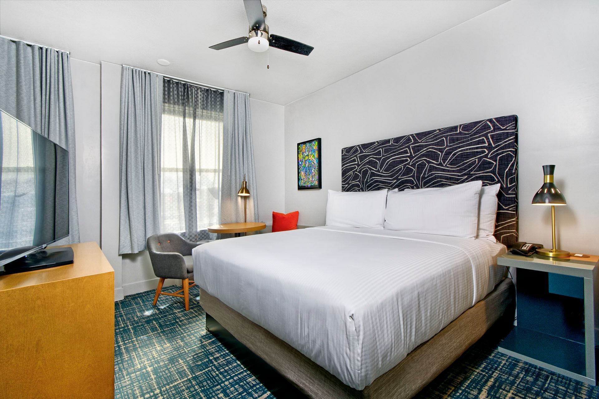 A hotel room with a large bed, nightstand, lamp, TV, and chair.