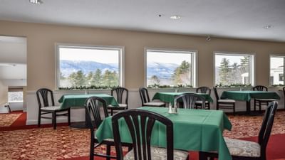 Dining area of the Fox Ridge Hotel with tables and chairs, large windows showing mountain view, and red carpeted floor.