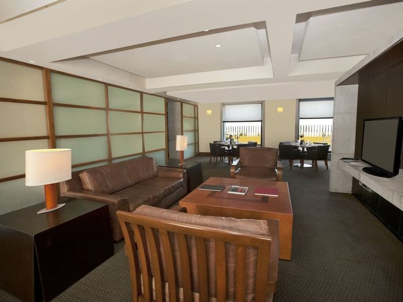 Lounge area with leather furniture, a wooden coffee table, a TV & dining space in Master Suite, 1 King at Grand Fiesta Americana