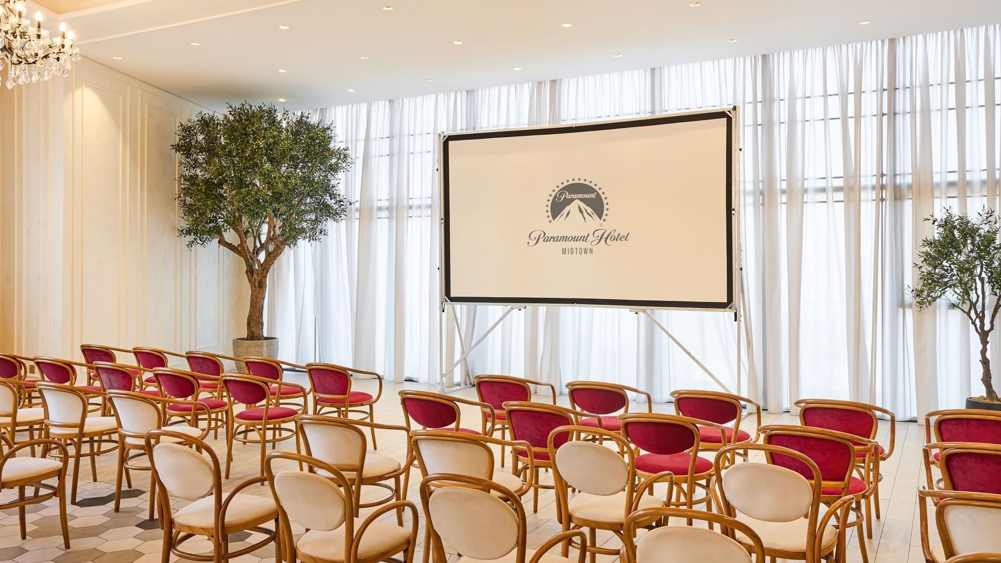 Auditorium-style seating arrangement facing a projector screen in Paparazzi restaurant venue at Paramount Hotel Midtown
