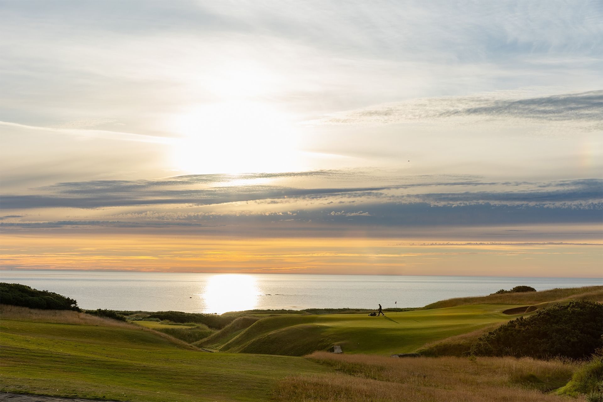 Golf course with players in the sunset, overlooking a calm sea near Luxury Hotels Fife