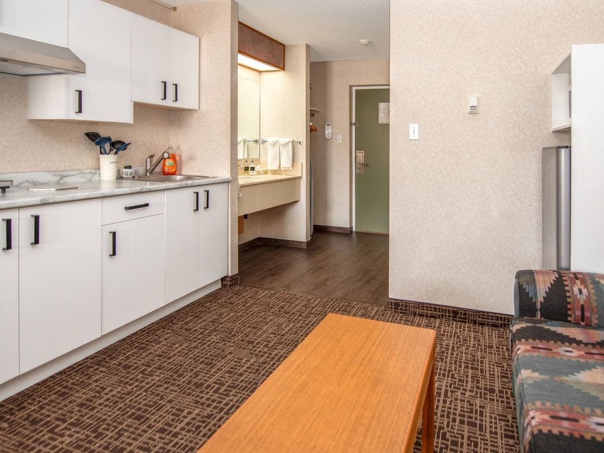 Living room with couch, coffee table, and kitchenette with white cabinets and appliances.
