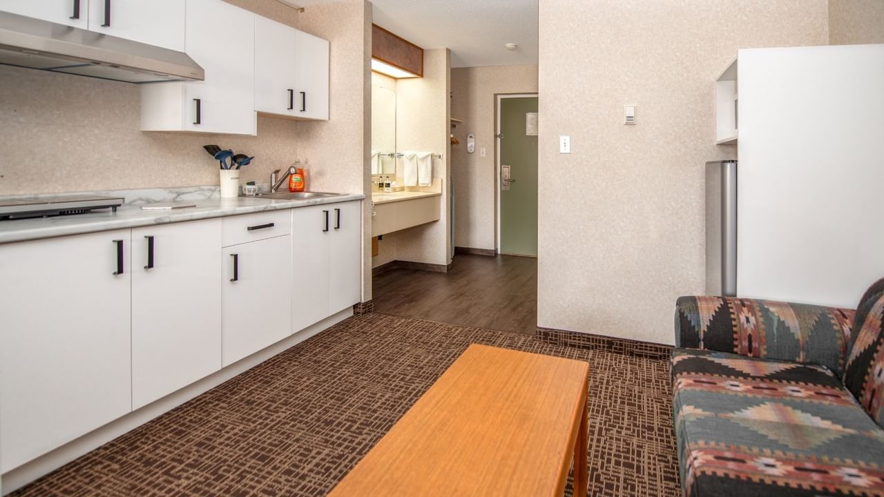 Living room with couch, coffee table, and kitchenette with white cabinets and appliances.